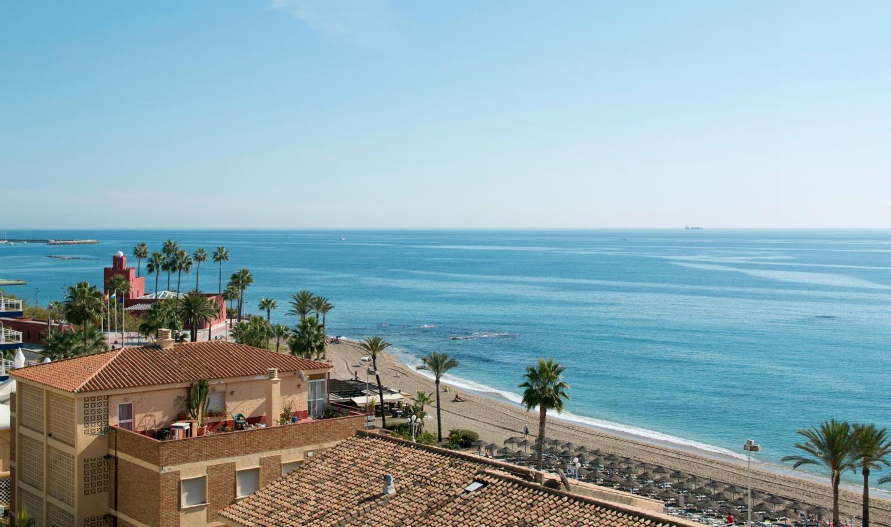 Skats no MedPlaya Hotel Alba Beach uz Vidusjūru un smilšu pludmali Benalmadenā, Spānijā — piekrastes ainava ar palmām un ēkām