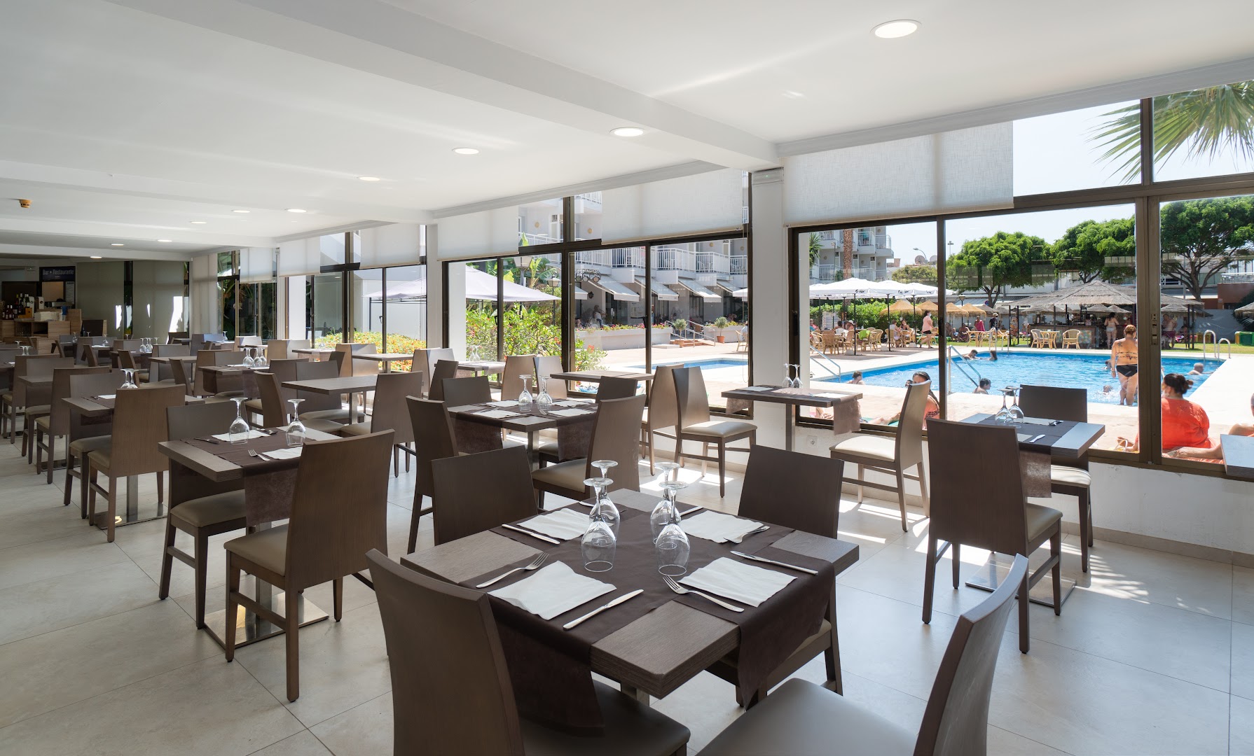 MedPlaya Hotel Alba Beach gaišā restorāna zāle ar skatu caur lielajiem logiem uz āra baseinu un atpūtas zonu
