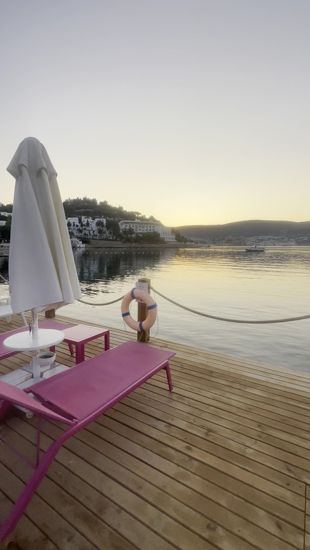 Prive Hotel Bodrum koka laipa ar rozā zviļņiem un saulessargu saulrieta laikā ar skatu uz līci