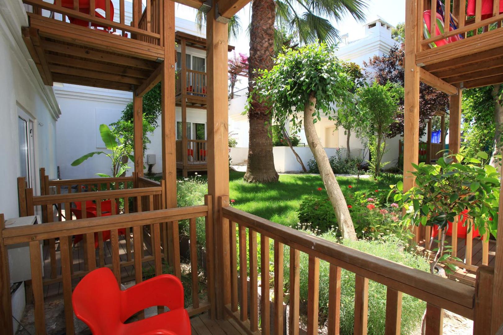Otium Senses Very Chic viesnīcas dārzs ar zaļu zālienu, palmām un koka bungalo tipa terasēm Bodrumā