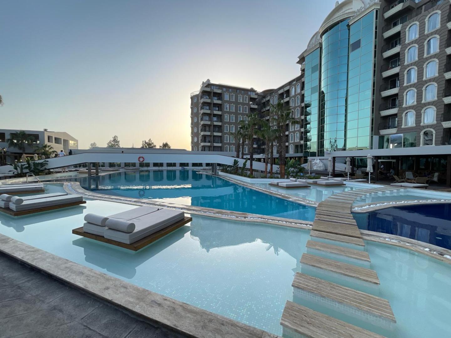 LAUR HOTELS Experience & Elegance āra baseins ar peldošiem sauļošanās krēsliem un viesnīcas ēku fonā Didimā, Turcijā saulrieta laikā