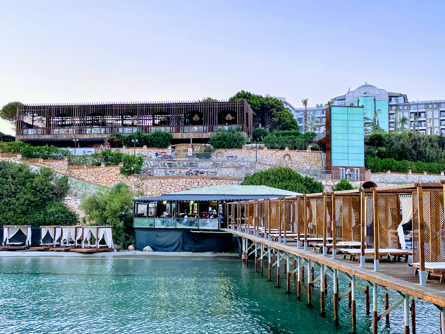 Laur Hotels Experience & Elegance skats uz pludmales bāru un koka laipu virs ūdens vakara gaismā Didimas piekrastē