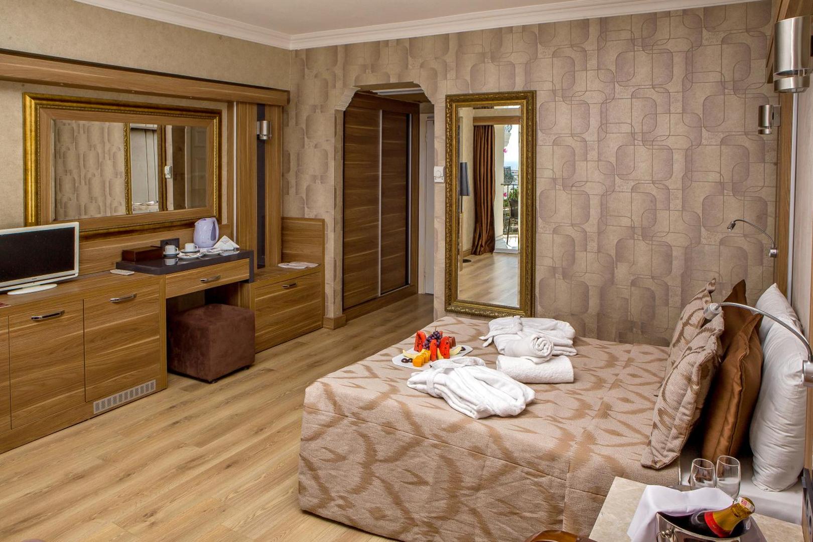 LAUR HOTELS Experience & Elegance numura interjers ar koka mēbelēm, lielu spoguli, darba zonu un sagatavotiem peldmēteļiem