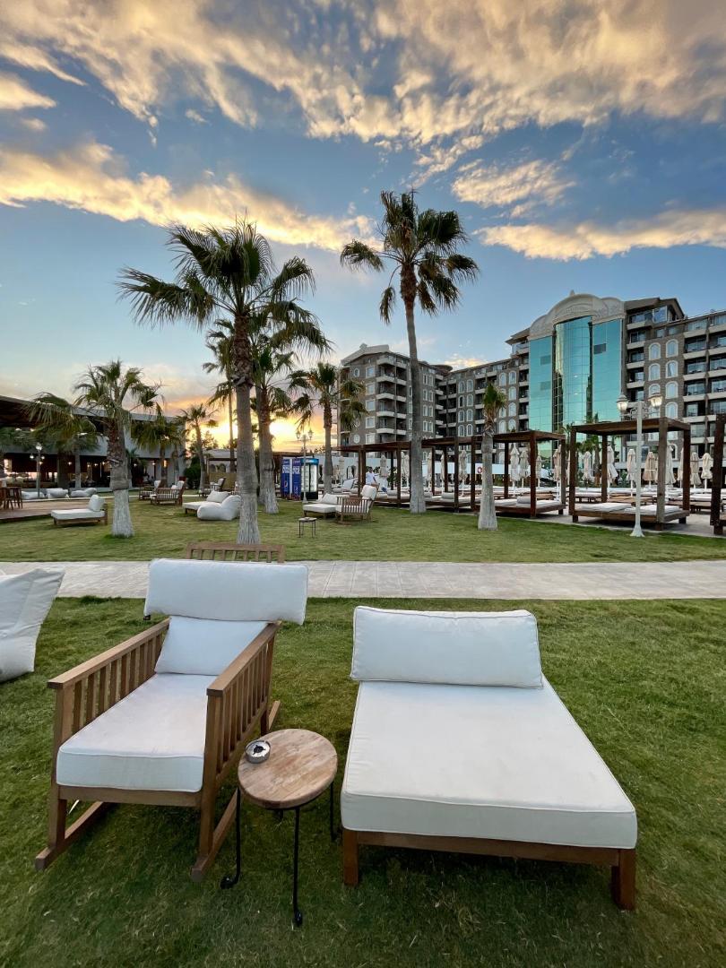 Viesnīcas LAUR HOTELS Experience & Elegance dārzs saulrietā ar palmām, zālāju, moderniem atpūtas krēsliem un ēkas fasādi