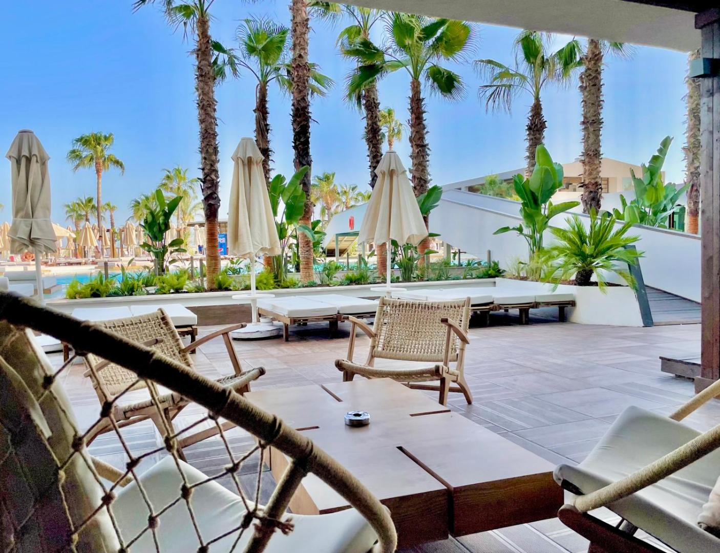 Viesnīcas Laur Hotels āra terase ar pītiem krēsliem, saulessargiem un skatu uz palmām un baseina zonu