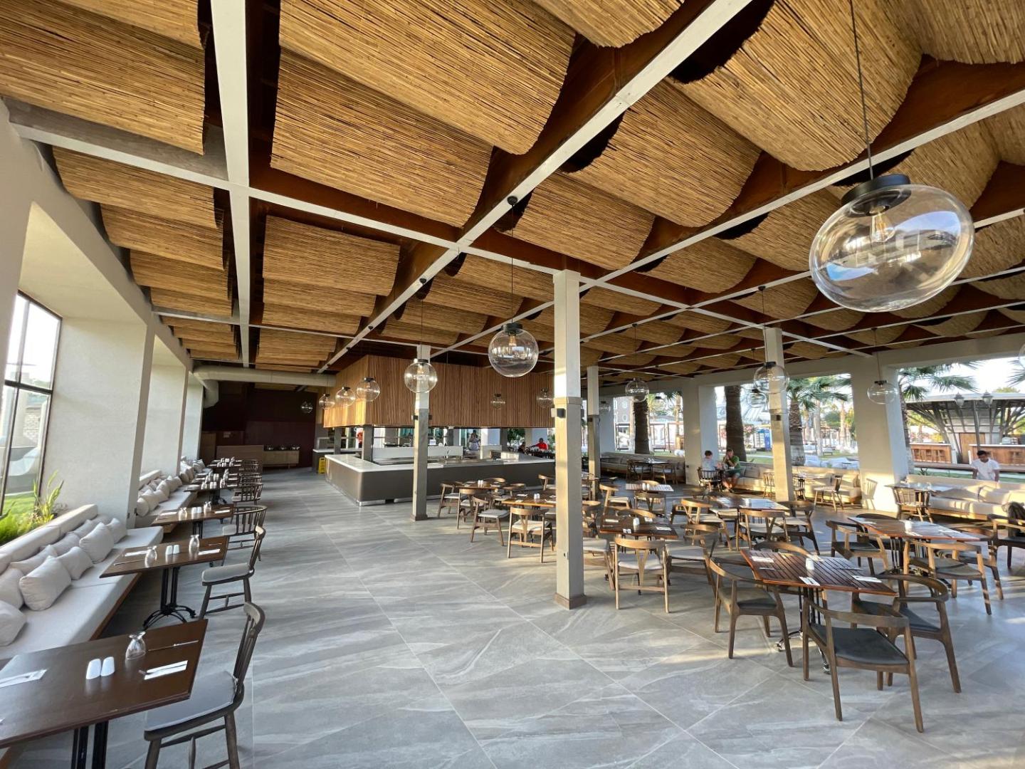 Plašs Laur Hotels Experience & Elegance viesnīcas restorāns ar ērtām mēbelēm, lieliem logiem un skatu uz palmu dārzu