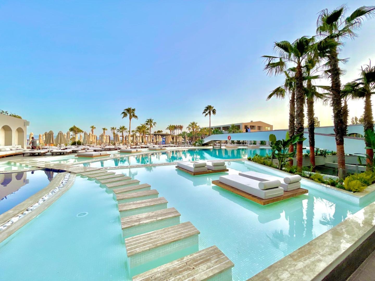 LAUR HOTELS Experience & Elegance plašā baseinu zona ar palmām, koka laipām un sauļošanās krēsliem zem skaidrām debesīm Didimas reģionā