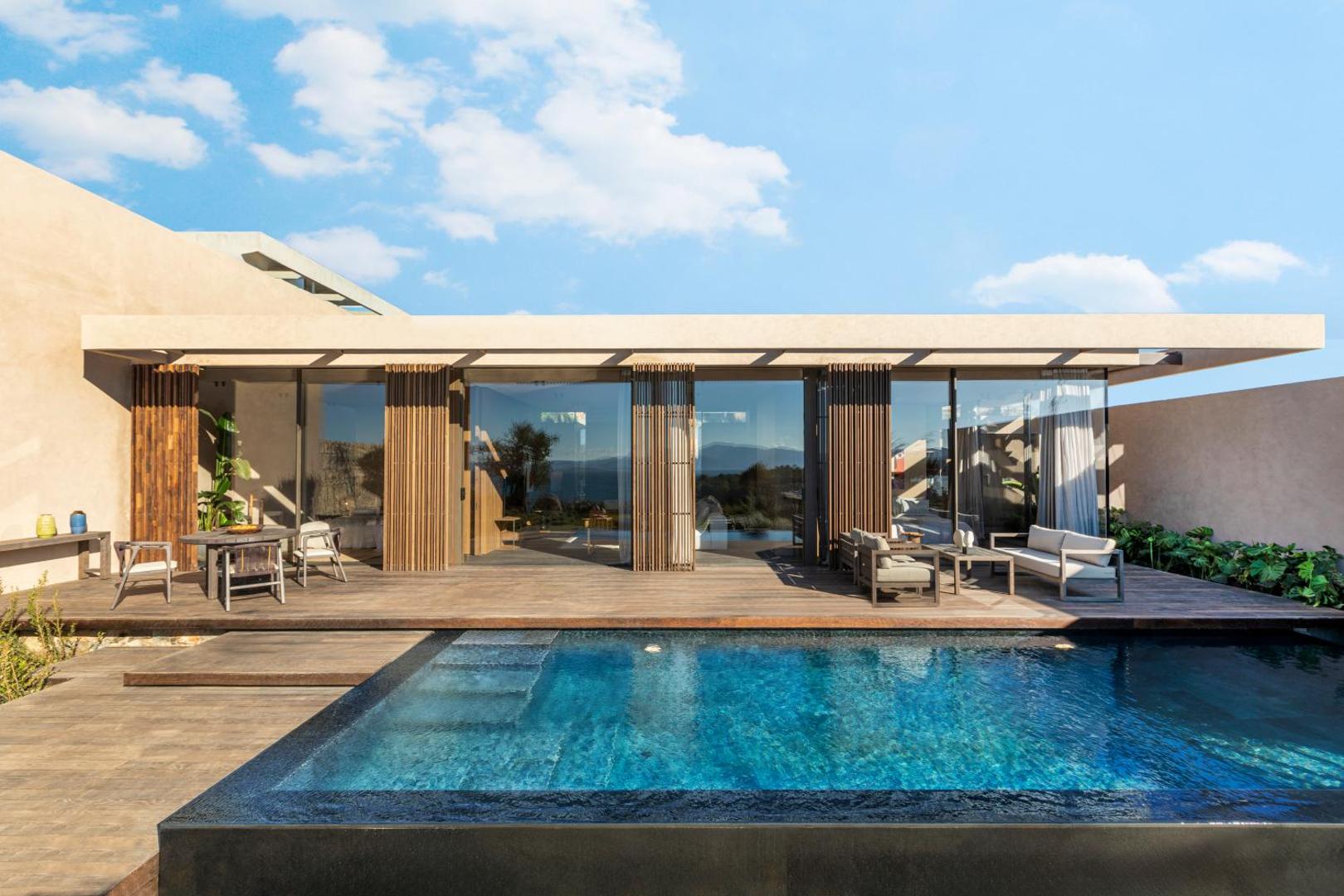 Lujo Hotel Bodrum moderna villa ar privātu baseinu, koka terasi un plašiem stiklotiem logiem saulainā dienā Bodrumas reģionā