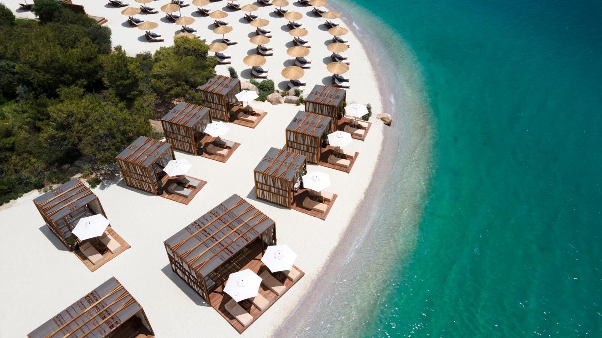 Lujo Hotel Bodrum privātā pludmale no putna lidojuma ar baltām smiltīm, saulessargiem un grezniem pludmales bungalo pie ūdens