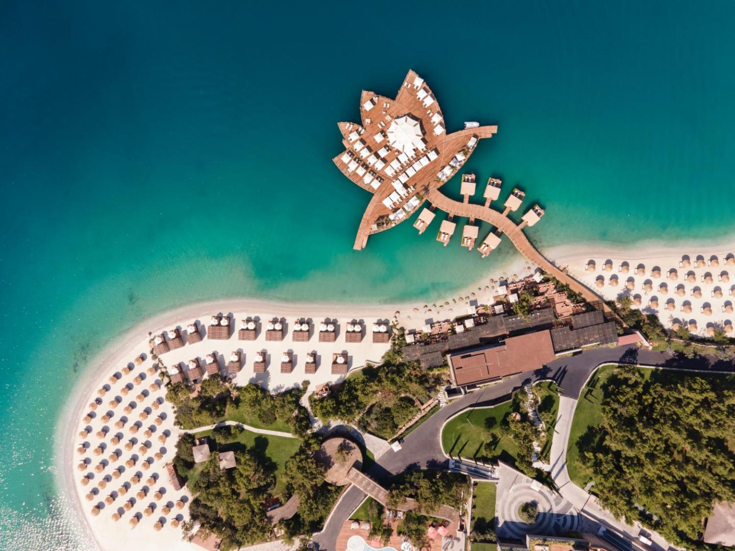 Lujo Hotel Bodrum skats no putna lidojuma uz unikālas formas koka laipu un privāto balto smilšu pludmali Egejas jūras piekrastē