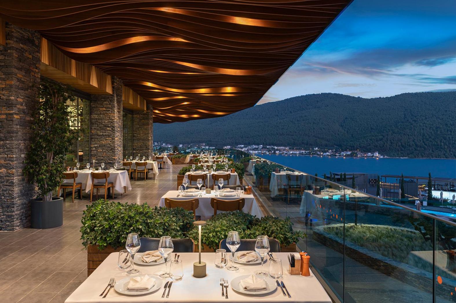 Lujo Hotel Bodrum elegants restorāns ar dizaina griestiem, akmens sienām un panorāmas skatu uz naksnīgo Bodrumas piekrasti
