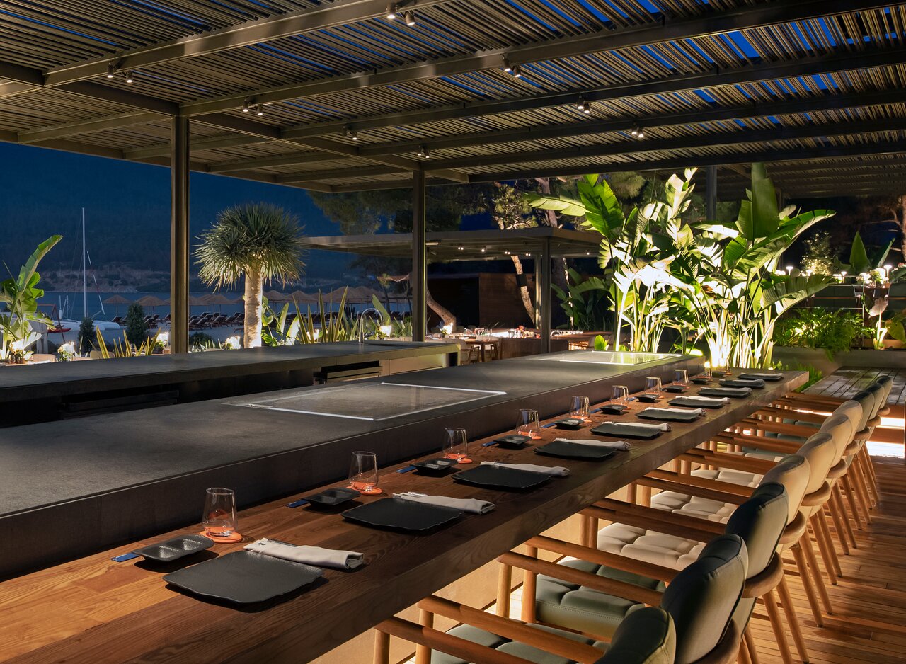Lujo Hotel Bodrum restorāna terase vakarā ar gariem koka galdiem, modernu apgaismojumu un skatu uz pludmali.