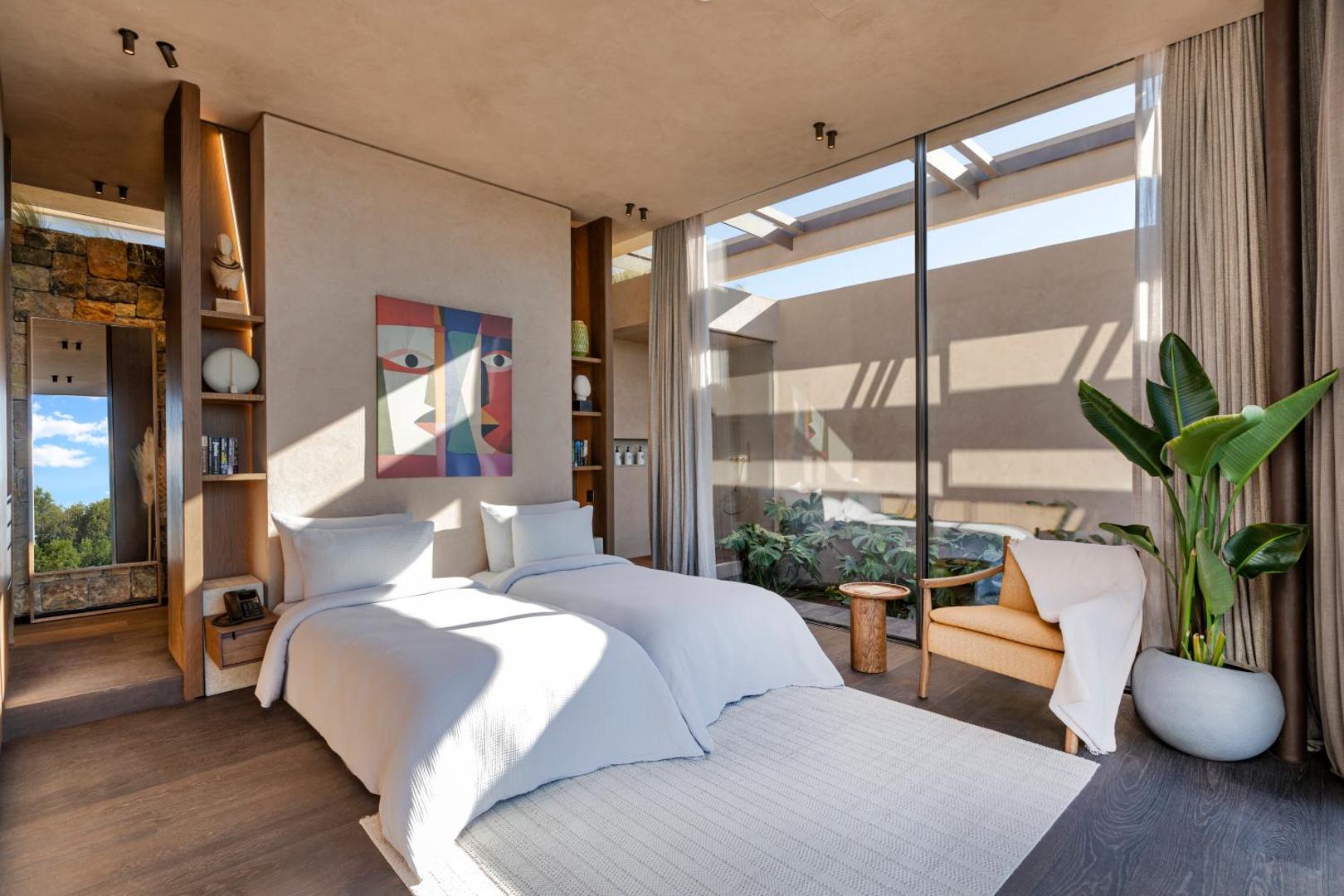 Lujo Hotel Bodrum moderns numurs ar divām gultām, siltu koka apdari, mākslas darbu pie sienas un lieliem logiem uz iekšpagalmu