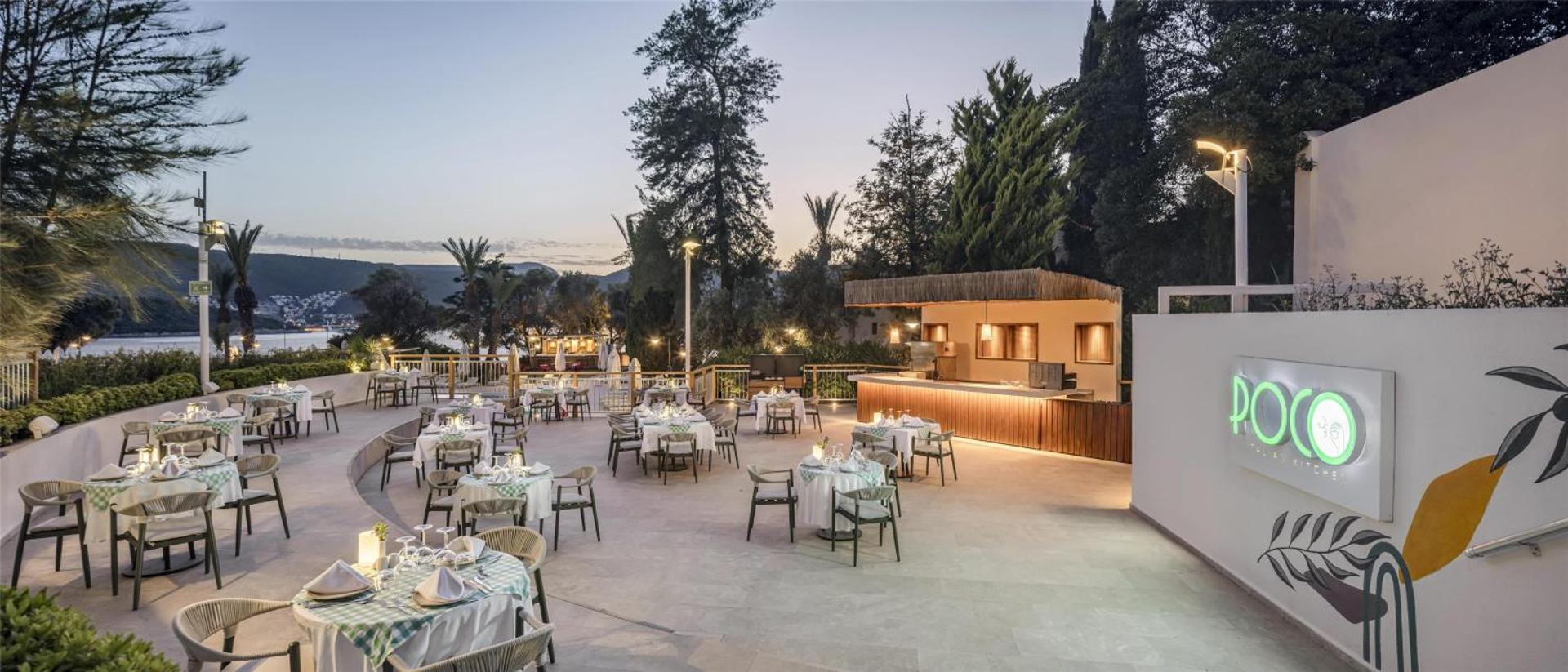 DoubleTree by Hilton Bodrum Isil Club Resort restorāns Poco ar āra terasi vakarā — eleganti klāti galdi un bāra zona priežu ielenkumā
