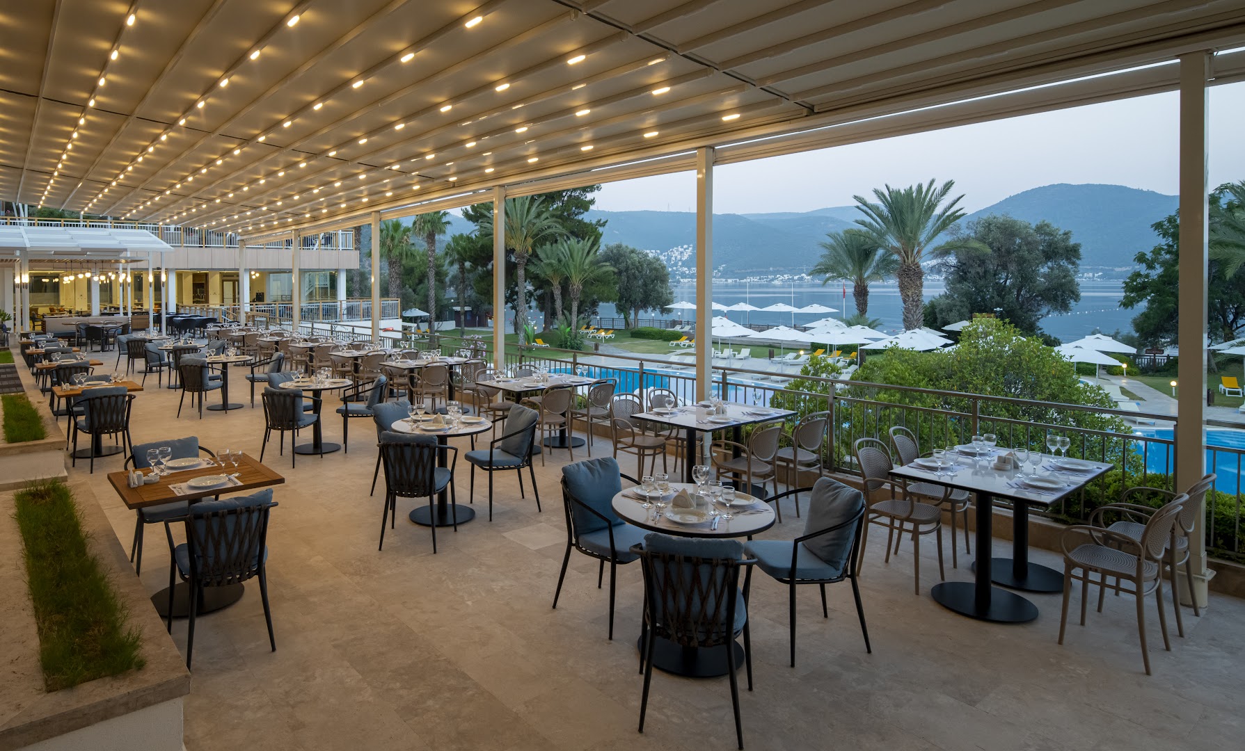 DoubleTree by Hilton Bodrum Isil Club Resort galvenā restorāna terase ar skatu uz jūru un baseinu — plaša ēdamzona zem nojumes