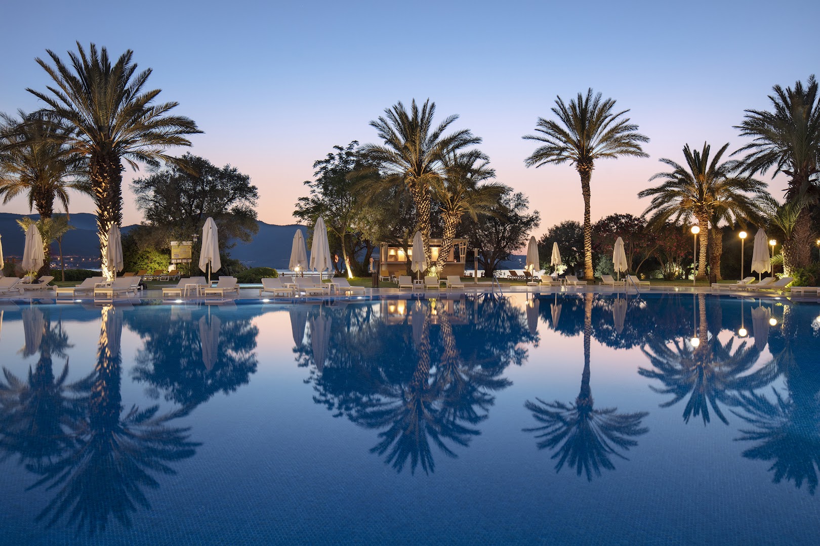 Tuvplāns DoubleTree by Hilton Bodrum Isil Club Resort baseinam saulrietā ar saulessargiem un palmām piekrastē