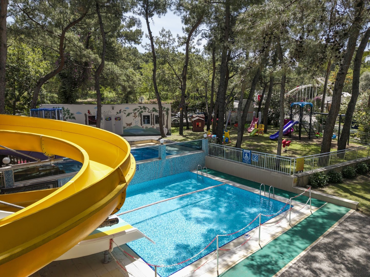 DoubleTree by Hilton Bodrum Isil Club Resort āra baseins ar dzeltenu spirālveida slidkalniņu un bērnu klubu fonā
