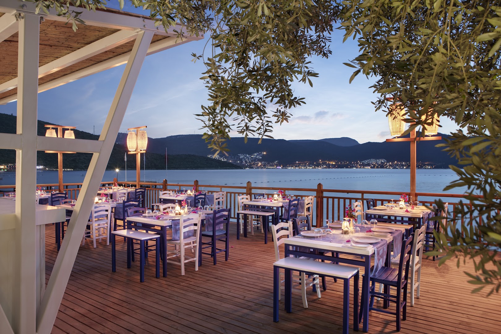 DoubleTree by Hilton Bodrum Isil Club Resort zivju restorāns Skorpina uz koka klāja pie jūras — zili balti galdi un laternas krēslā