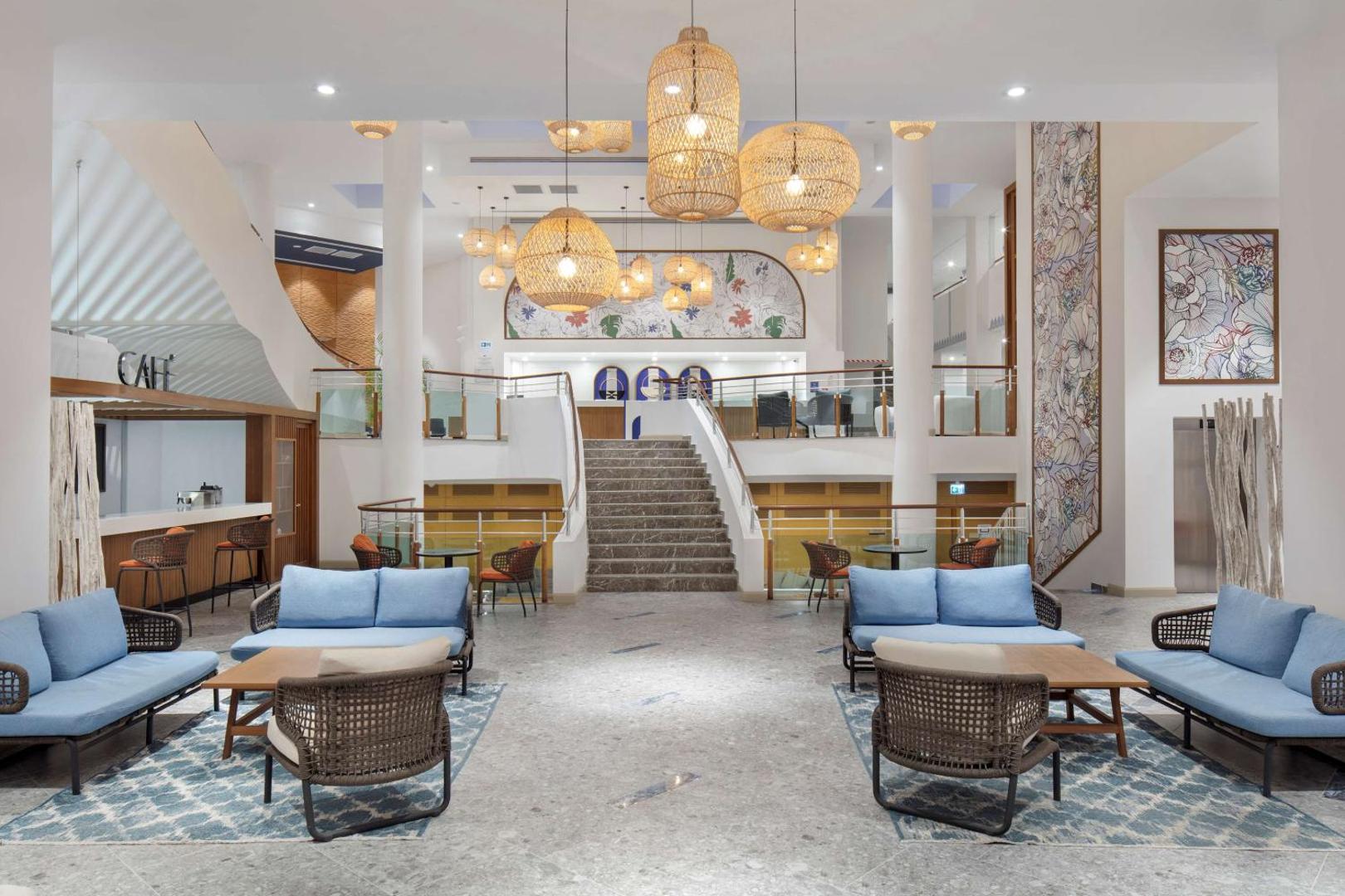 DoubleTree by Hilton Bodrum Isil Club Resort plašais vestibils ar modernām mēbelēm, pītiem gaismekļiem un centrālajām kāpnēm Bodrumas piekrastē