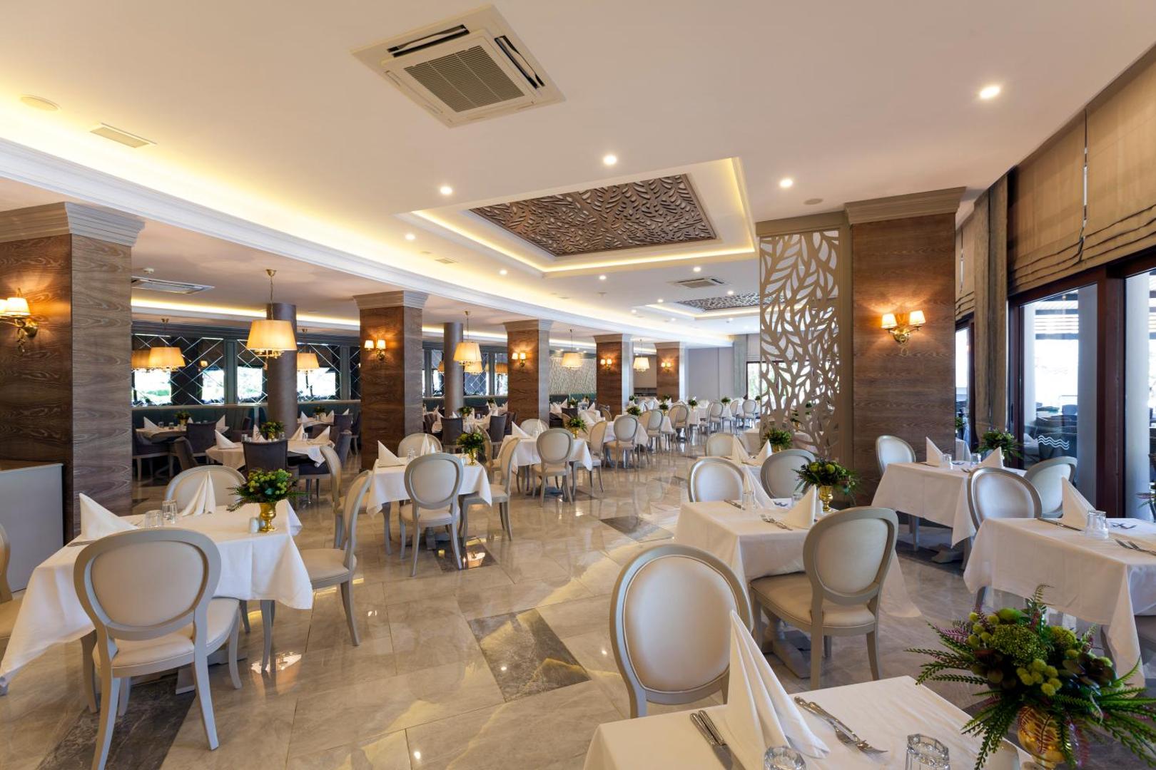 Samara Hotel Bodrum galvenais restorāns ar elegantiem galdiem, baltiem galdautiem un dekoratīviem griestu elementiem