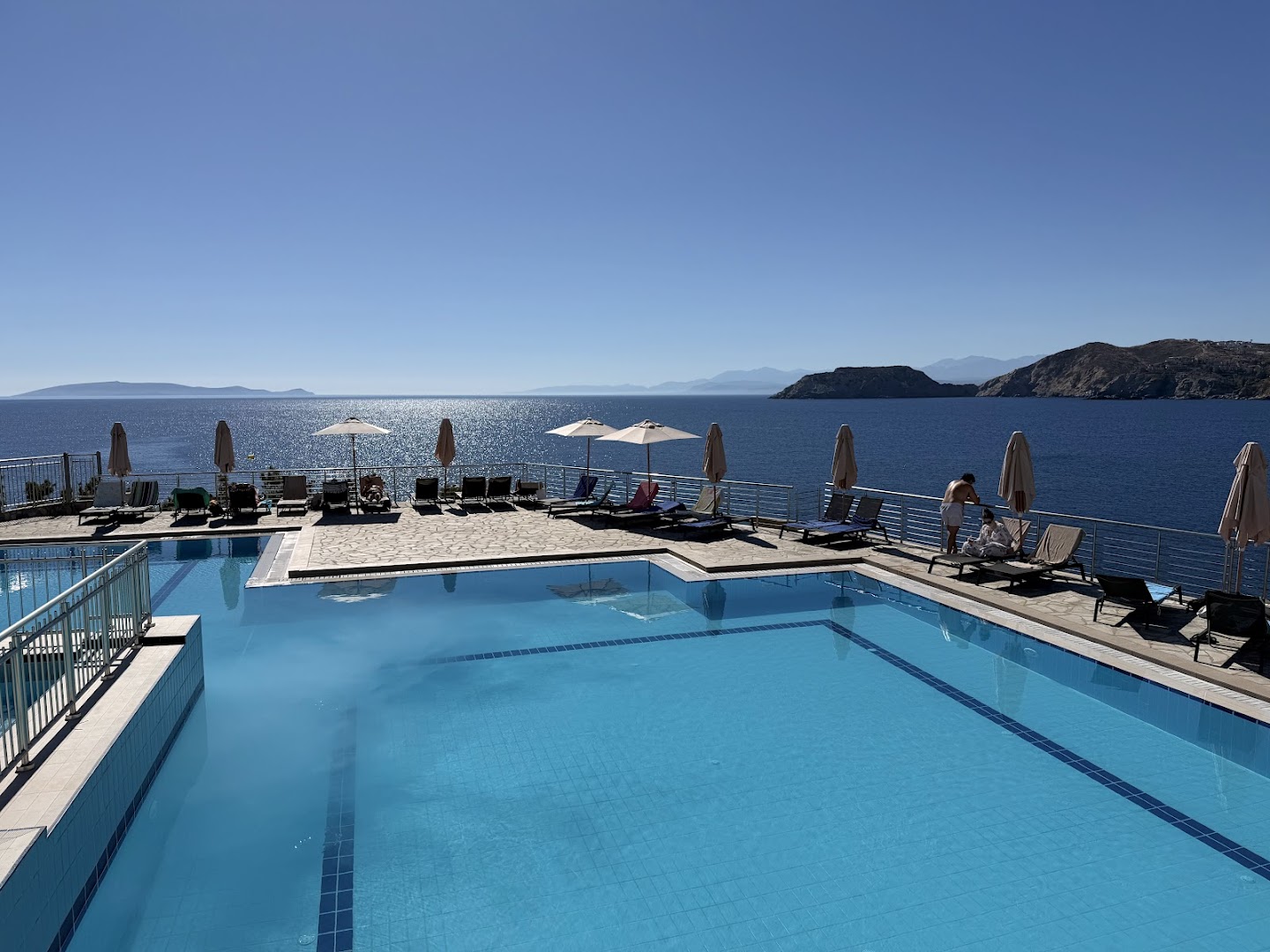 Peninsula Resort & Spa āra baseins ar skatu uz jūru Agia Pelagia, Krētā — sauļošanās terase ar krēsliem un saulessargiem