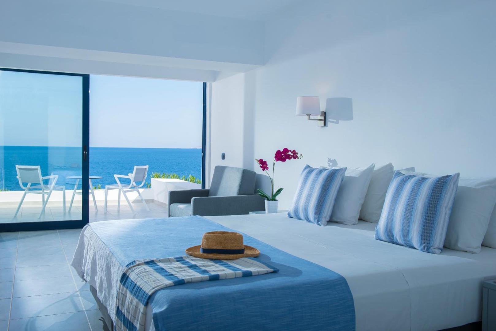 Peninsula Resort & Spa moderns numurs ar panorāmas logu uz Vidusjūru Krētā — terase ar krēsliem un mājīgs interjers
