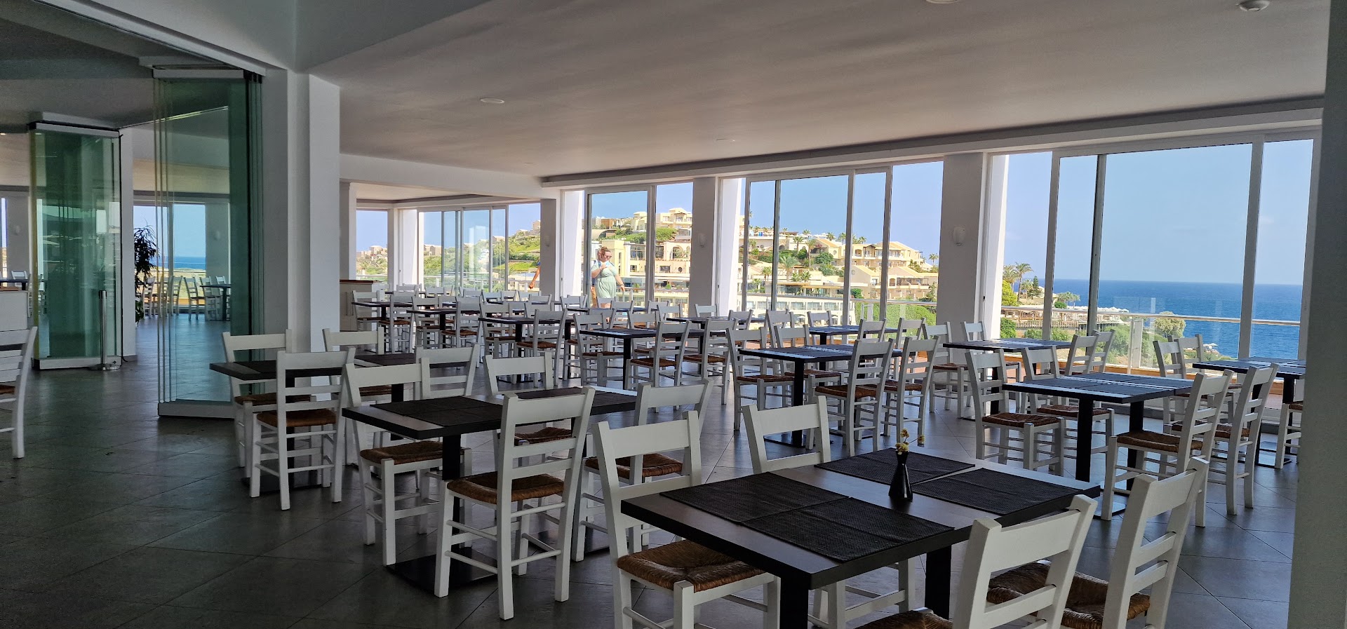 Peninsula Resort & Spa plašais iekštelpu restorāns ar lieliem logiem, no kuriem paveras skats uz kūrorta ciematu un jūru