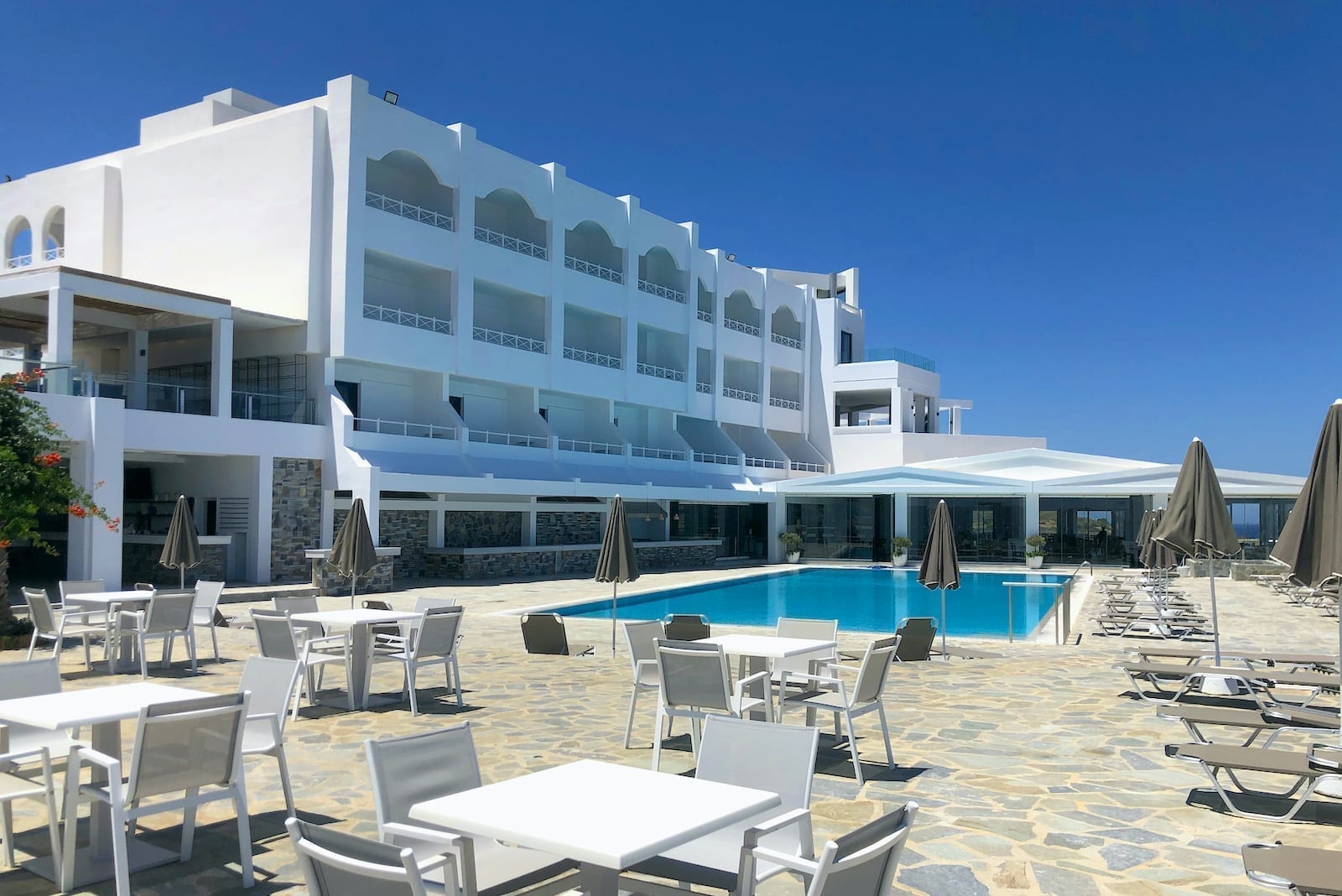 Peninsula Resort & Spa viesnīcas ēka ar balkoniem, āra baseinu un atpūtas zonu ar galdiņiem un krēsliem Krētā