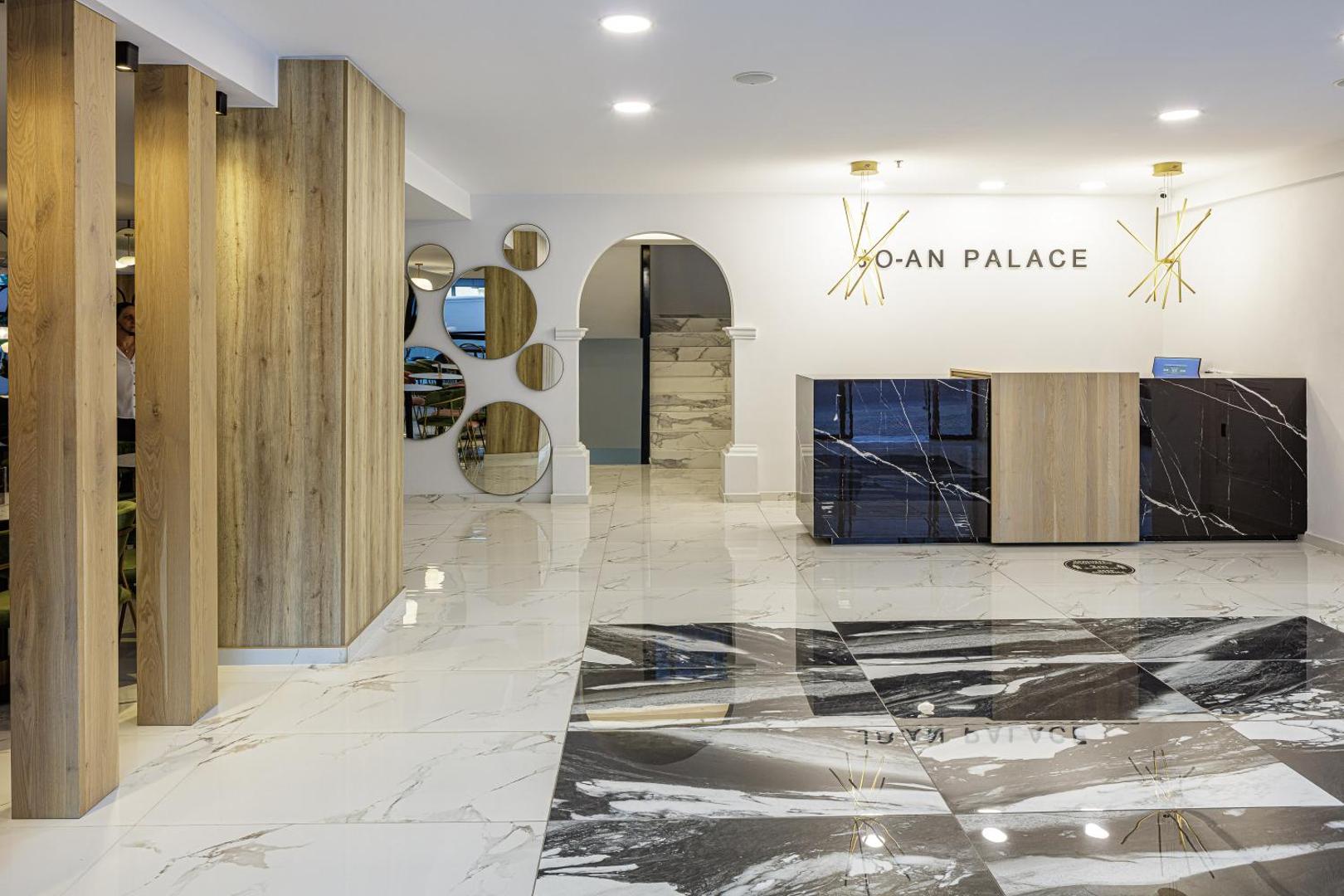 Joan Palace viesnīcas recepcijas zona ar marmora grīdu un modernu dizainu — gaišs vestibils ar koka elementiem un spoguļu dekorācijām