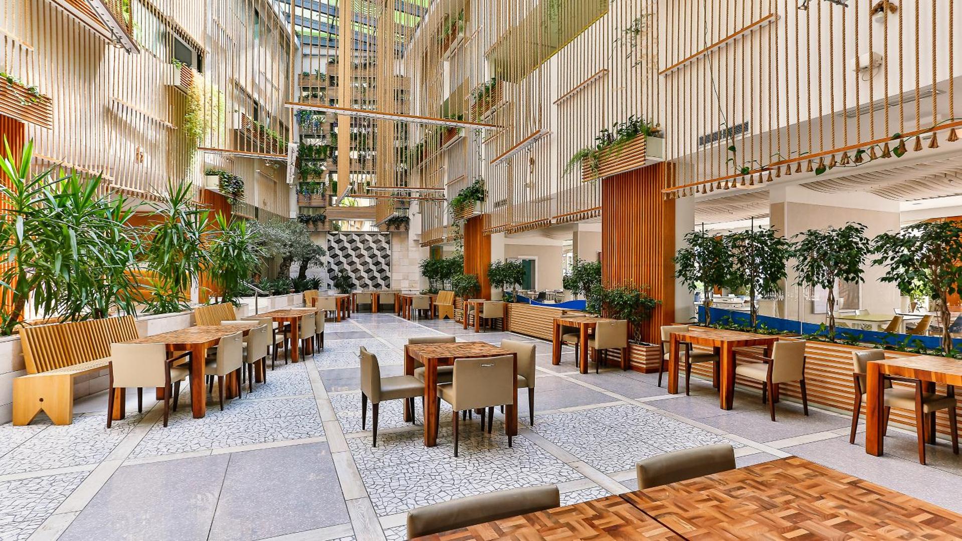 Viesnīcas Carine Hotel Park plašā atpūtas zona un restorāns ar dizaina mēbelēm un dekoratīviem zaļumiem