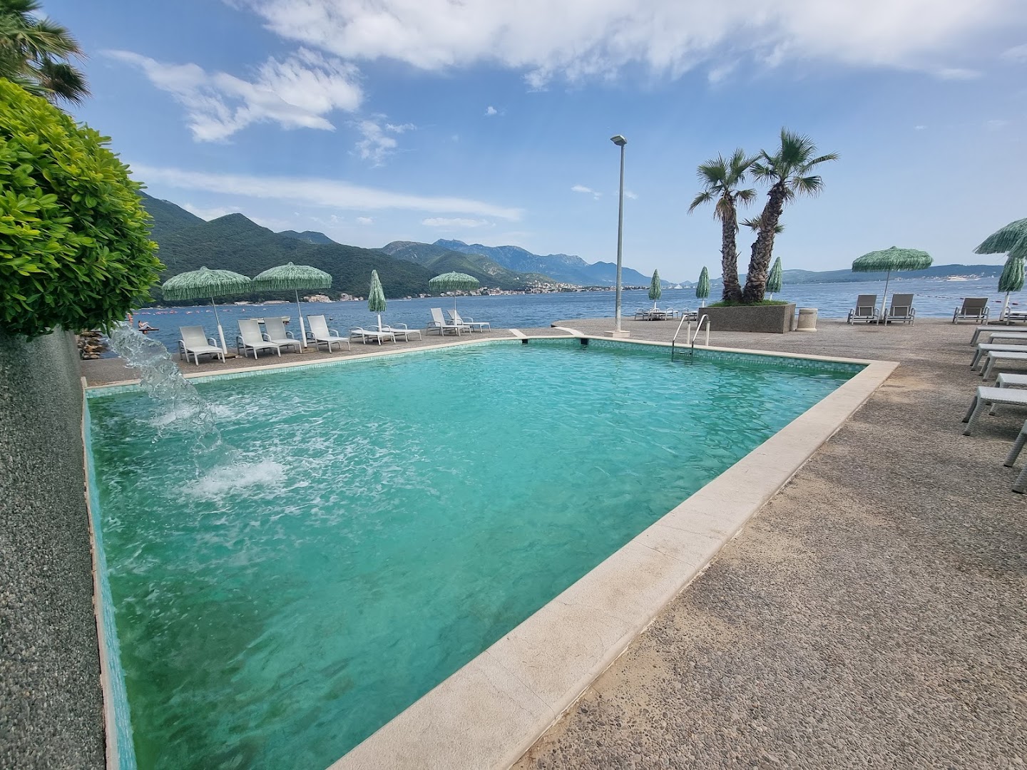 Carine Hotel Park baseins tiešā jūras tuvumā ar skatu uz kalniem — saulessargi un sauļošanās krēsli piekrastes zonā