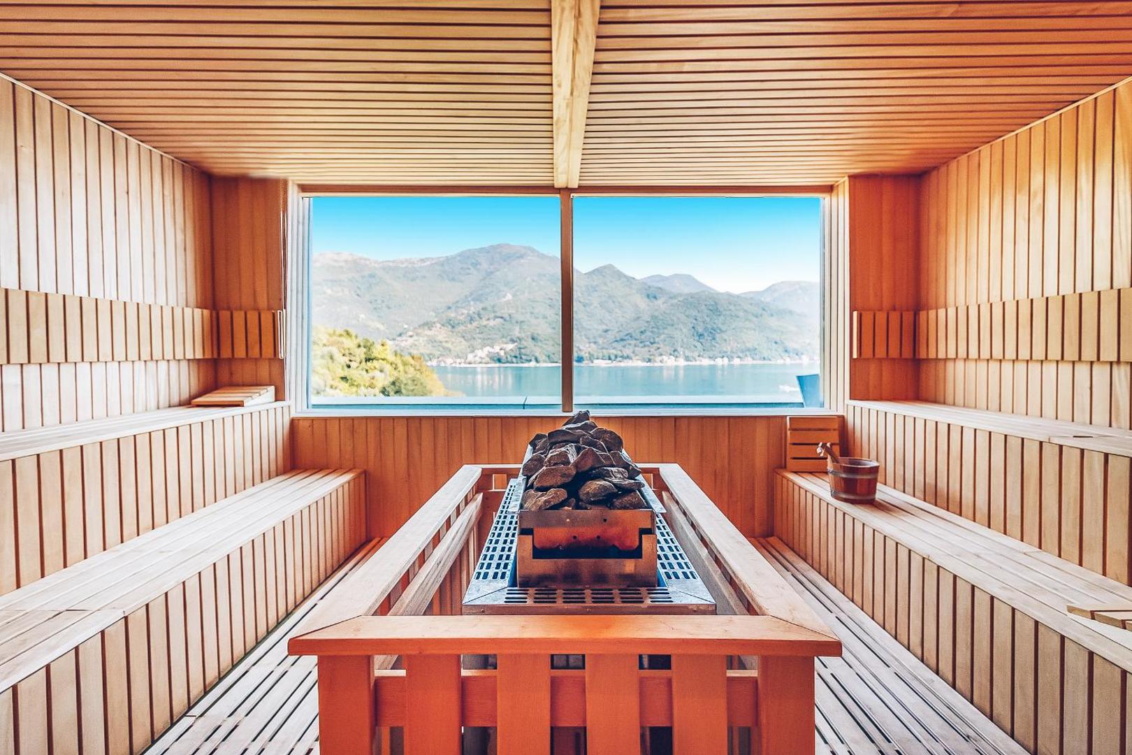 Carine Hotel Park spa zonas sauna ar panorāmas logu uz Kotoras līci Melnkalnē — koka apdare un akmens krāsns centrā