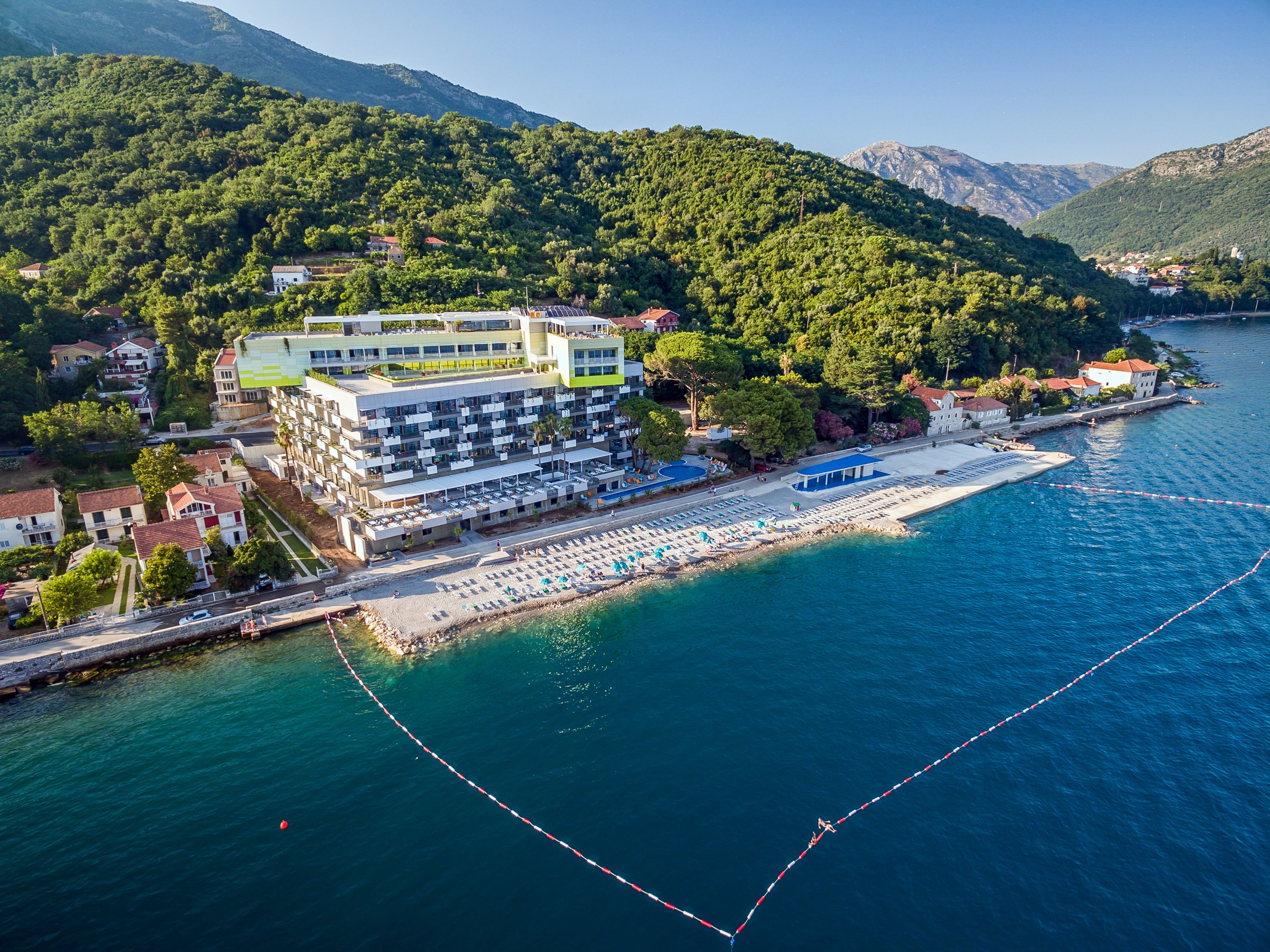 Carine Hotel Park skats no putna lidojuma Bijelā, Melnkalnē — viesnīcas ēka tieši pie Adrijas jūras krasta ar privātu pludmali