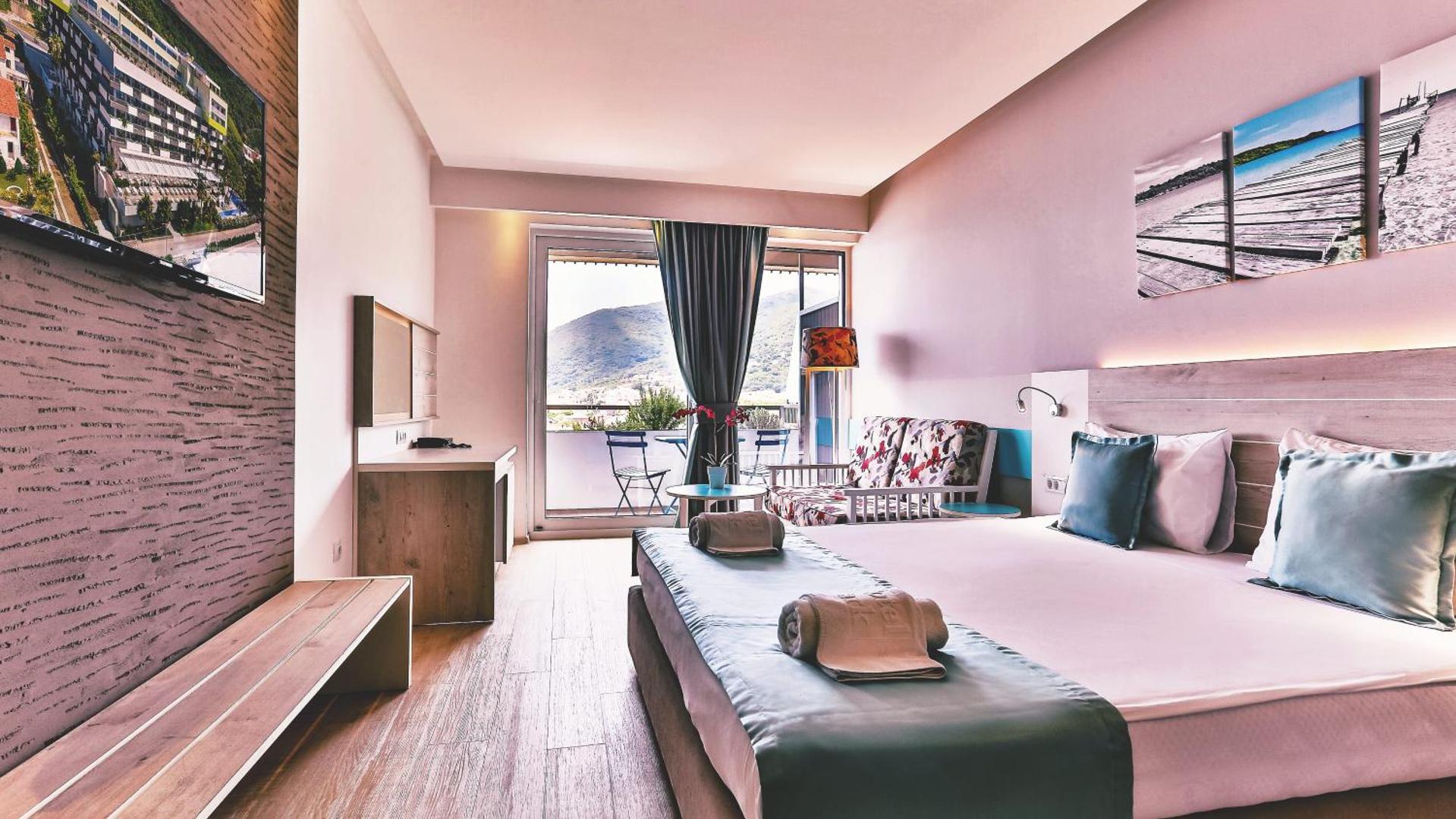 Gaišs Carine Hotel Park viesnīcas numurs ar balkonu, no kura paveras skats uz Melnkalnes kalniem un piekrasti
