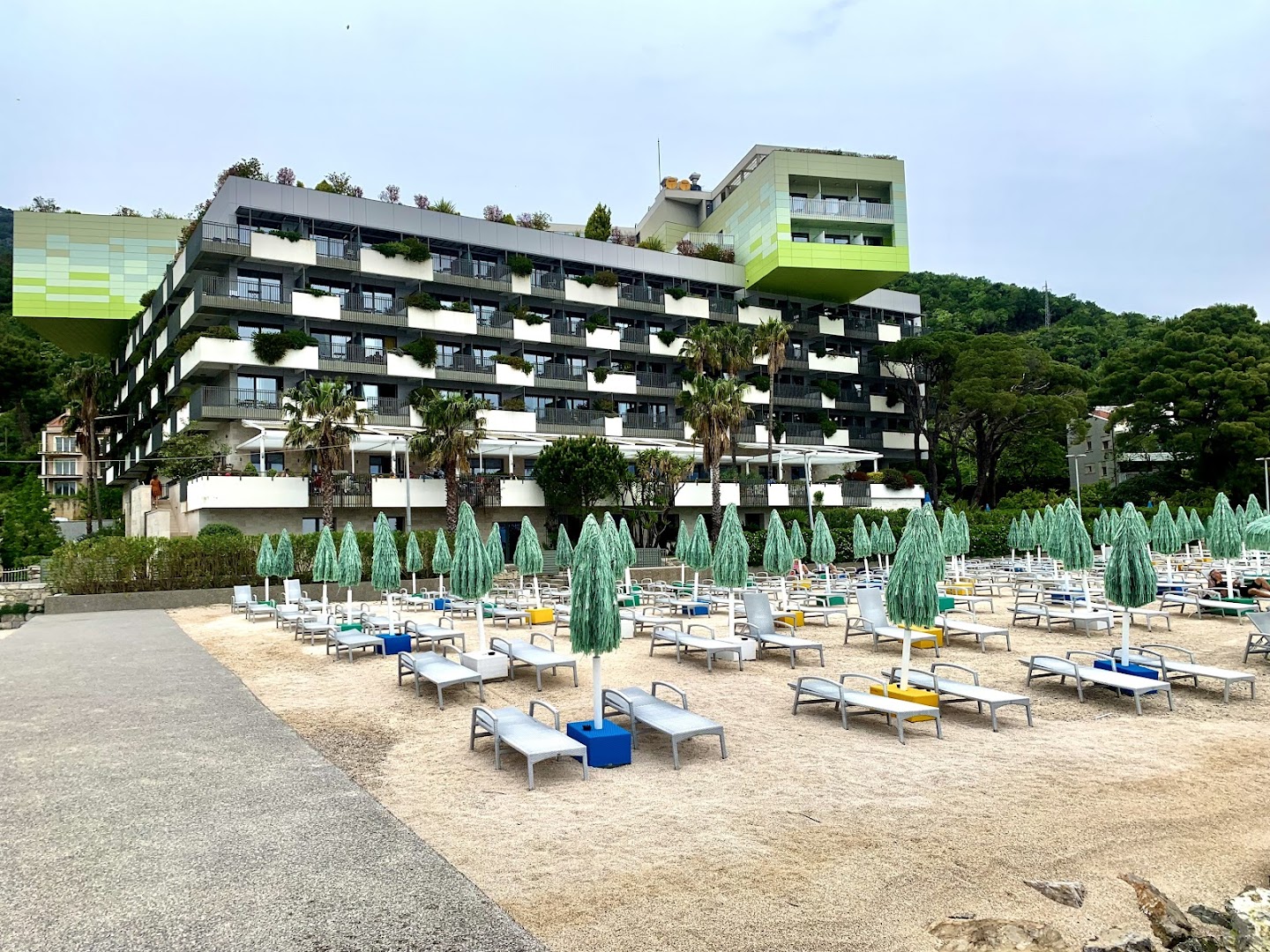 Carine Hotel Park modernā arhitektūra un fasāde Bijelā ar pludmales zonu priekšplānā un zaļojošiem kalniem fonā