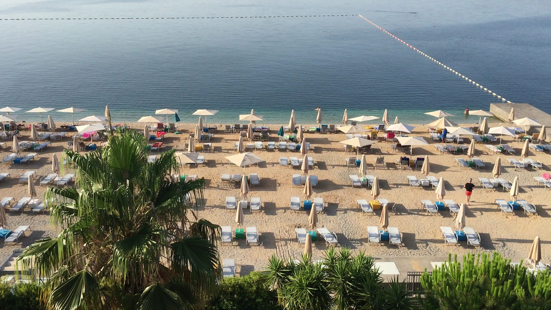 Carine Hotel Park privātā pludmale Bijelā, Melnkalnē — skats no augšas uz saulessargiem, zviļņiem un dzidro Adrijas jūras līci