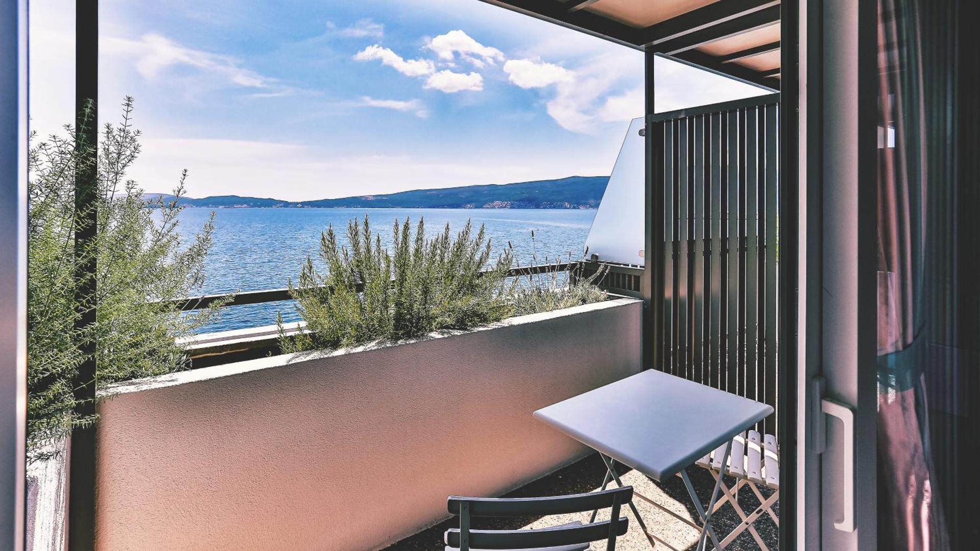 Skats no Carine Hotel Park privātā balkona uz Kotoras līča zilo ūdeni un kalnu grēdām saulainā dienā