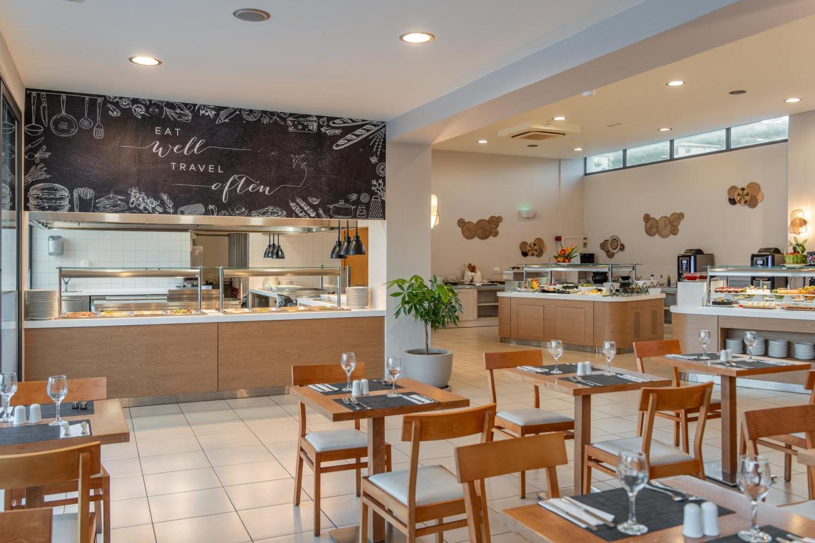 Ariadne Beach viesnīcas restorāna iekštelpas ar koka galdiem, krēsliem un bufetes līniju modernā stilā