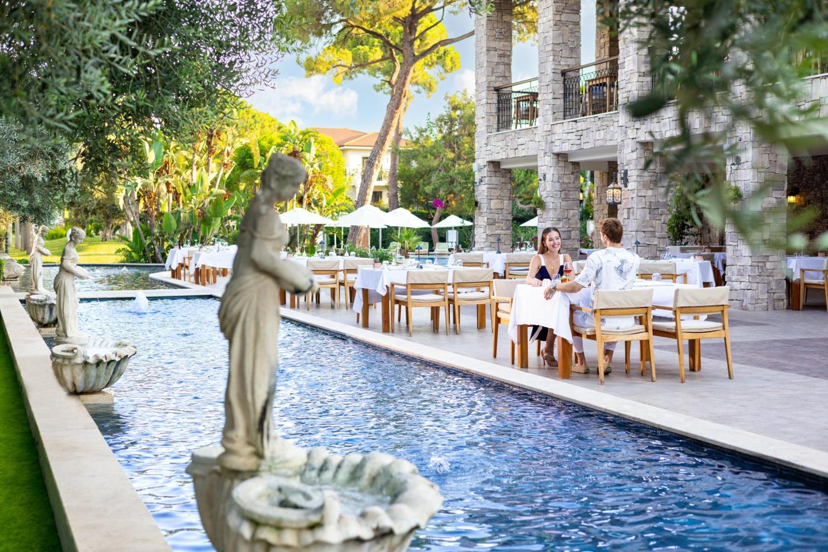 Pāris bauda pusdienas Ela Excellence Resort Belek āra restorānā pie dekoratīva baseina ar skulptūrām un dārza fonu