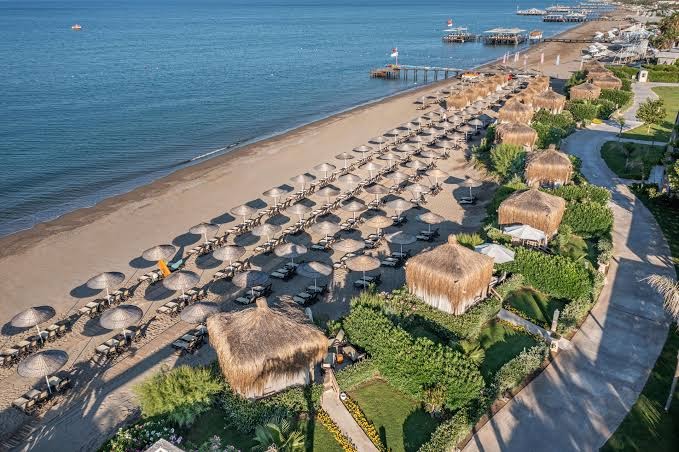 Ela Excellence Resort Belek privātā pludmale no putna lidojuma ar saulessargiem, sauļošanās krēsliem un bungalo pie jūras