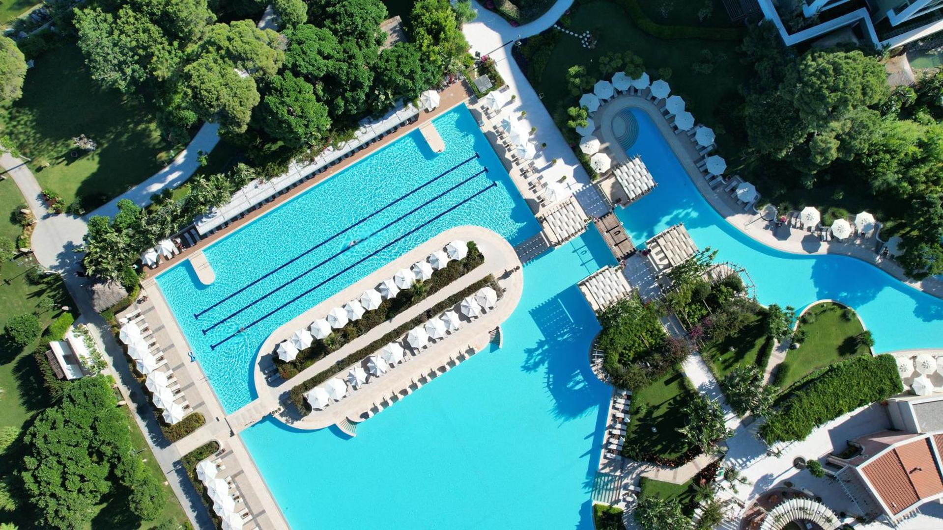Ela Excellence Resort Belek plašā āra baseinu sistēma no putna lidojuma, ko ieskauj zaļš dārzs un atpūtas zonas Belekā