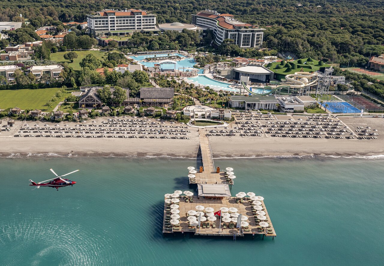 Ela Excellence Resort Belek skats no putna lidojuma uz viesnīcas teritoriju, baseiniem, privāto pludmali un koka piestātni ar atpūtas zonu Belekā.