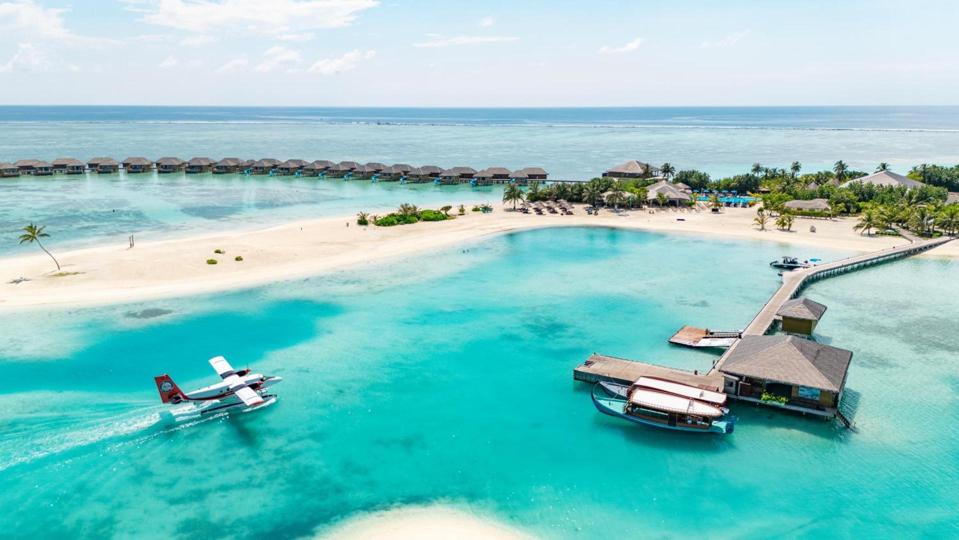 Cocoon Maldives kūrorta panorāma ar lagūnu, piestātni, hidroplānu un ūdens bungalo rindu tālumā