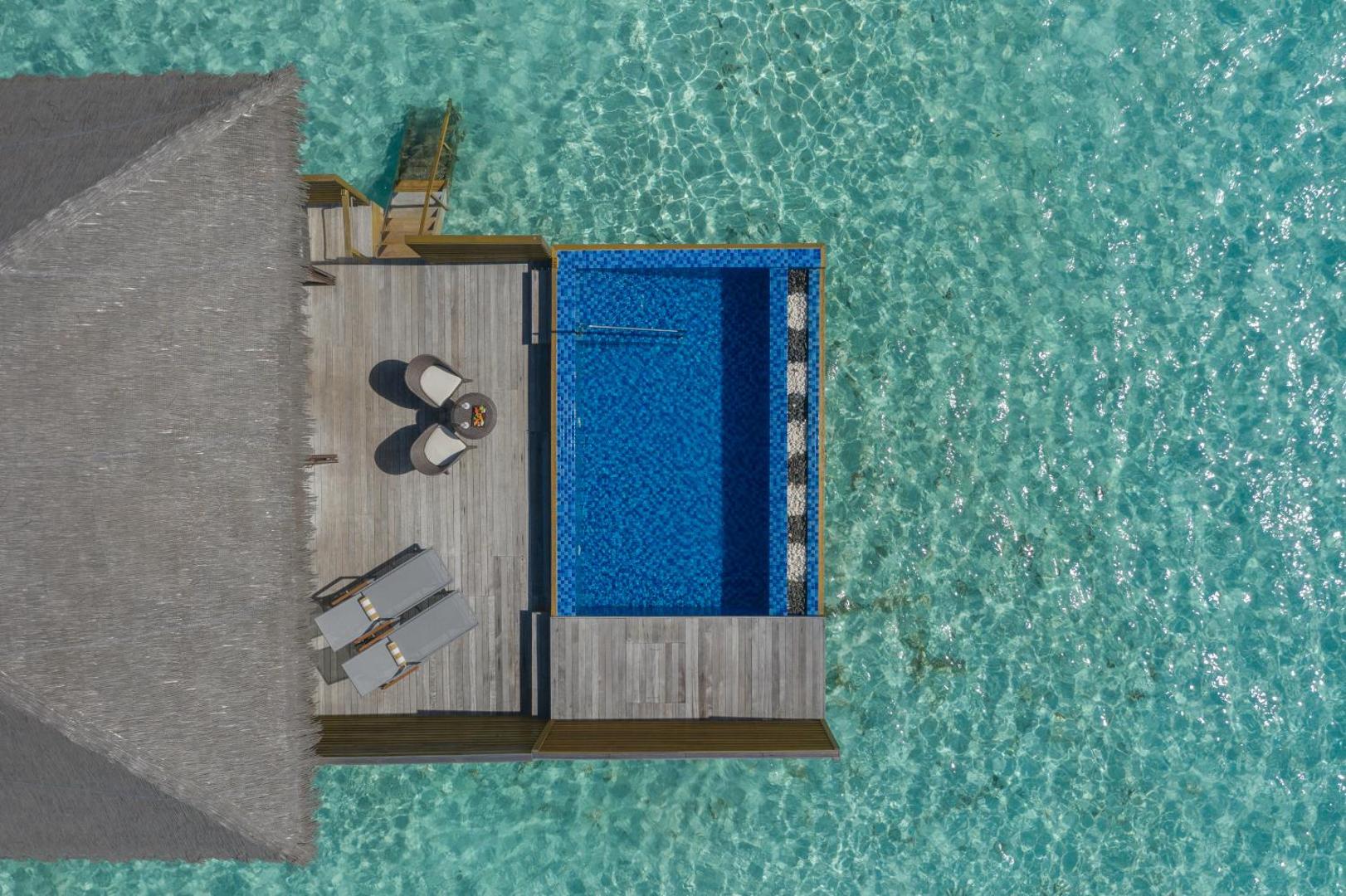 Cocoon Maldives ūdens bungalo terase ar privātu baseinu, sauļošanās krēsliem un tiešu skatu uz tirkīzzilo okeānu no augšas