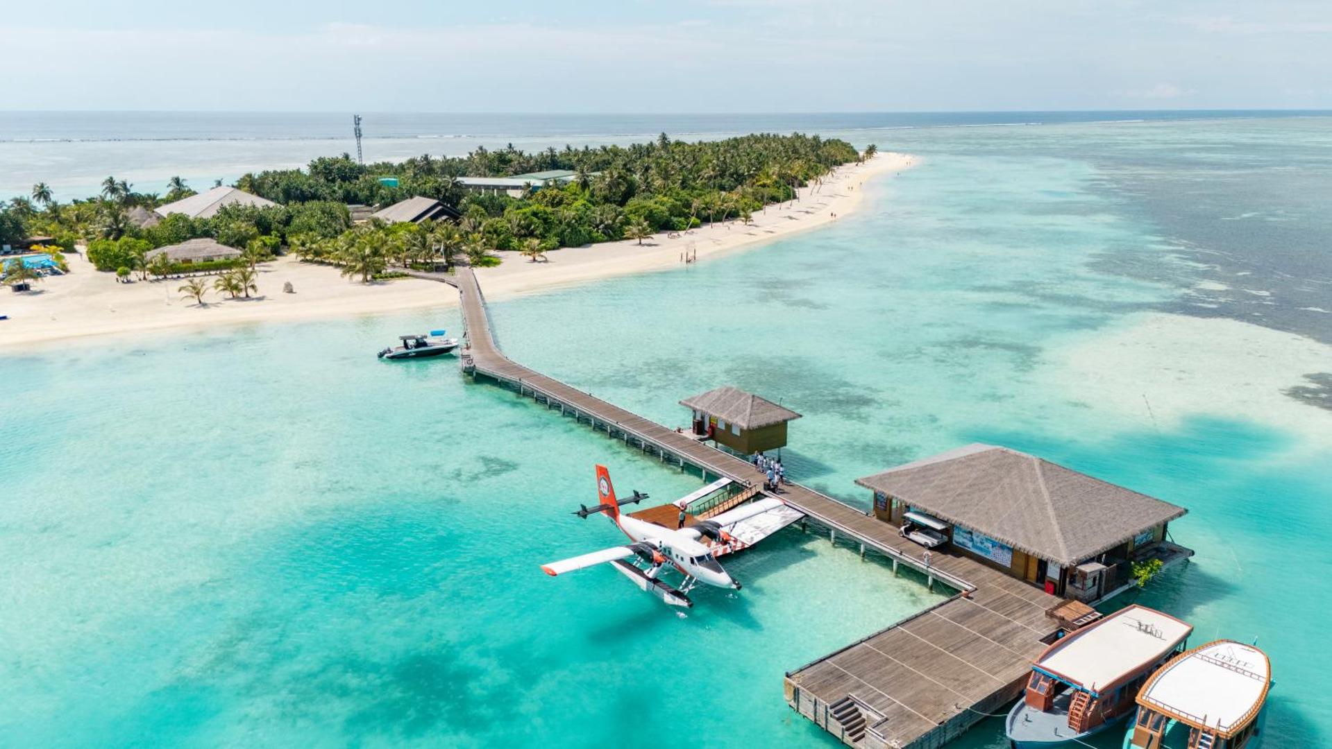 Cocoon Maldives kūrorta skats no putna lidojuma uz koka piestātni, hidroplānu un tirkīzzilo lagūnu pie salas krasta