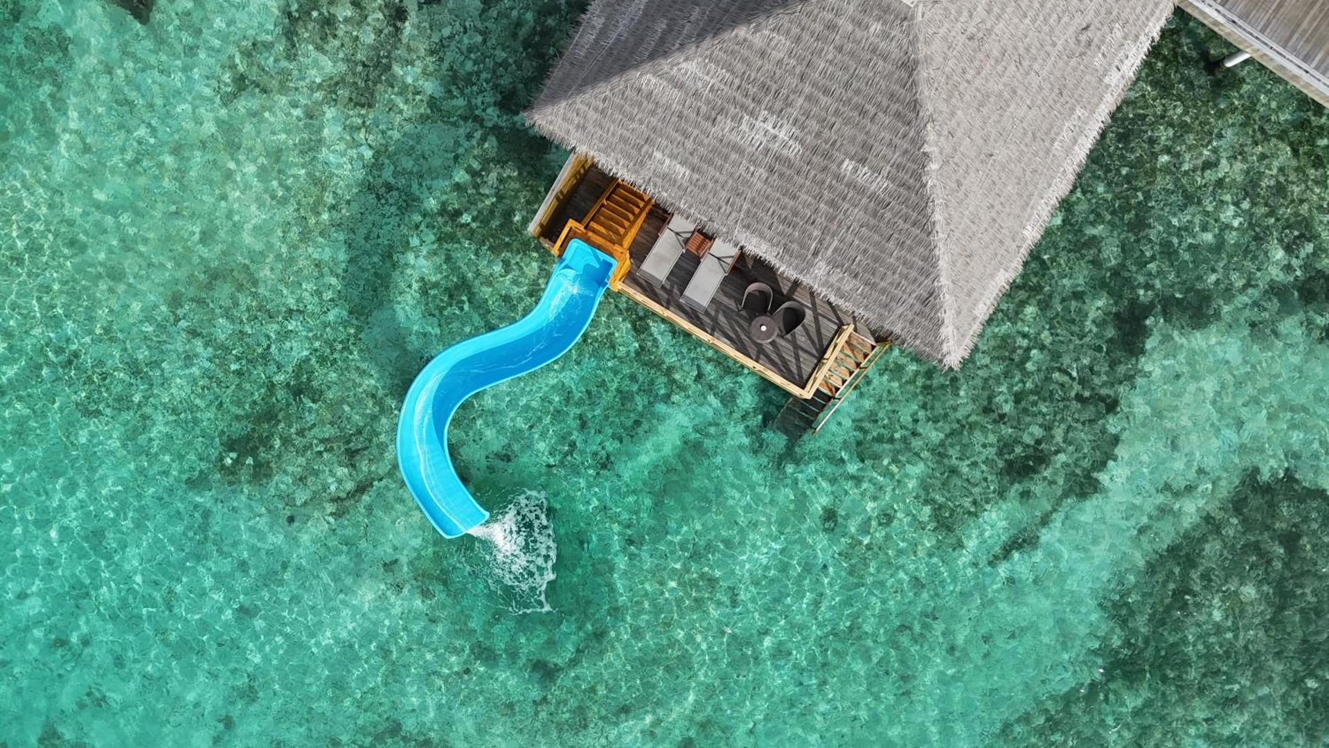 Cocoon Maldives ūdens bungalo terase ar privātu ūdens slidkalniņu, kas ved tieši tirkīzzilajā okeāna ūdenī