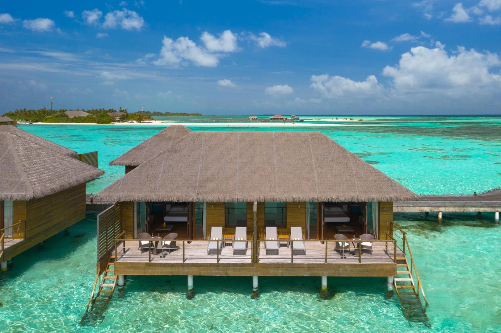 Cocoon Maldives bungalo virs ūdens ar salmu jumtiem un koka terasēm tirkīza krāsas okeāna piekrastē Maldīvu salās