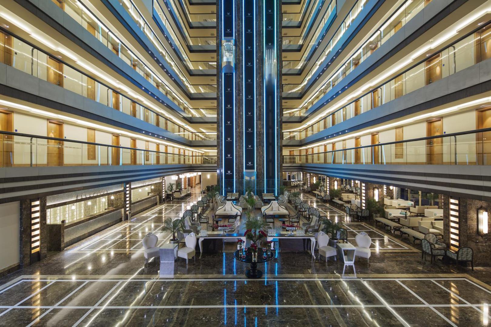 Liberty Hotels Lara centrālais vestibils ar moderniem liftiem un marmora grīdu — skats uz atpūtas zonu un recepciju