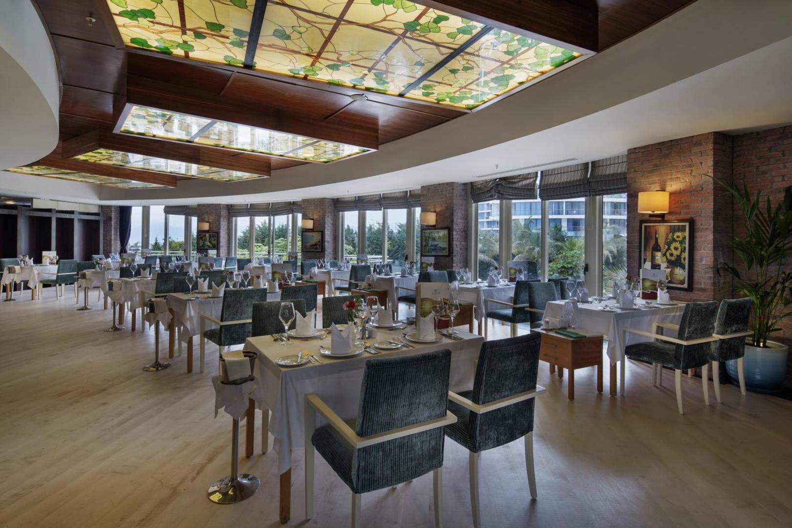 Liberty Hotels Lara moderns restorāns ar vitrāžas griestiem un ķieģeļu sienu apdari — gaišs interjers un mīkstie krēsli