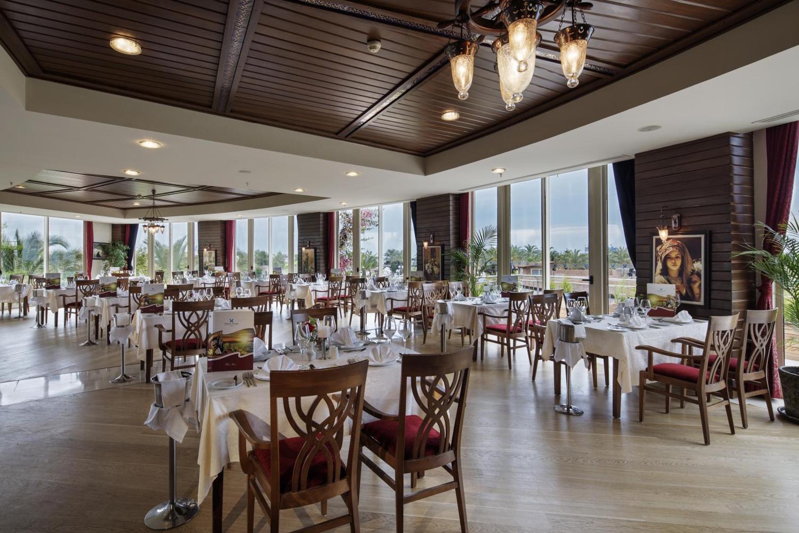 Liberty Hotels Lara restorāns ar klasisku koka interjeru un lieliem logiem — eleganti klāti galdi un skats uz dārzu